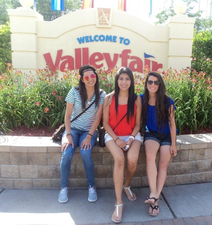 Andrea and two other young women sitting in front of a large sign that reads "Welcome to Valleyfair"