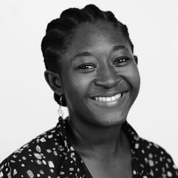 A portrait of ama benewaa tawiah. in this black and white photo she is wearing her hair in cornrows, a floral print blouse, and a wide smile.