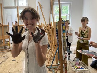 High school student with paint on her hands surrounded by easels