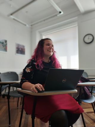 Woman with pink hair sitting at desk with laptop