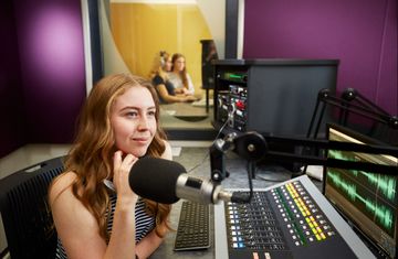 A female intern sits in front of a studio A/V board while recording 