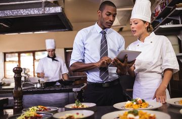 A restaurant manager reviews information on a table with a chef