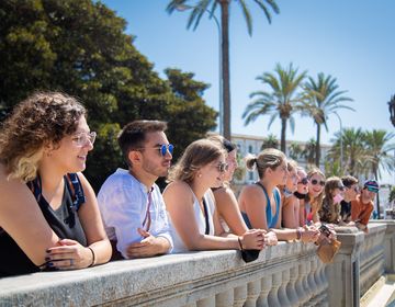 Students leaning on a balustrade facing La Caleta Beach in Cadiz