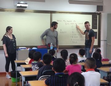 Teachers in front of a class of students pointing at a whiteboard