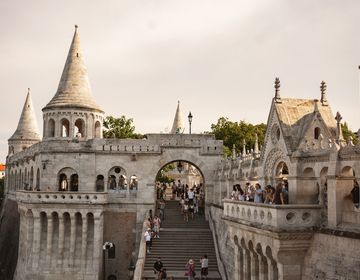 Tourists stroll through the elaborate Fisherman's Bastion in Budapest, admiring the unique towers and enjoying the beautiful evening light.