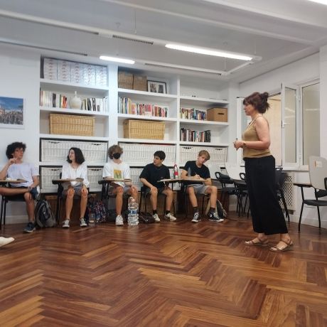 Teacher giving lecture to students sitting at desks against wall