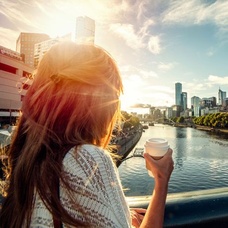 young woman drinking coffee on a bridge over a river in melbourne