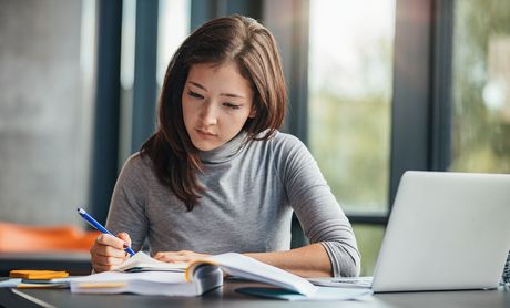 Woman writing in a notebook with her laptop open beside her