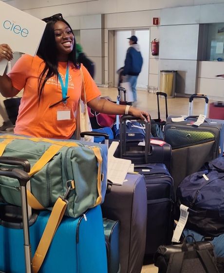 Young woman holding up CIEE sign in airport, surrounded by suitcases