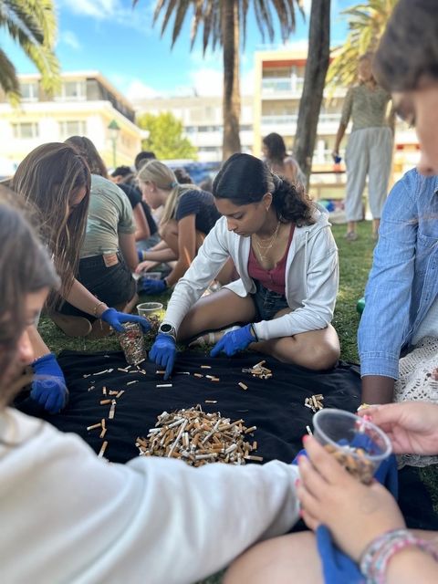 Students sit around a black towel placing cigarette butts into a shape with blue protective gloves. 