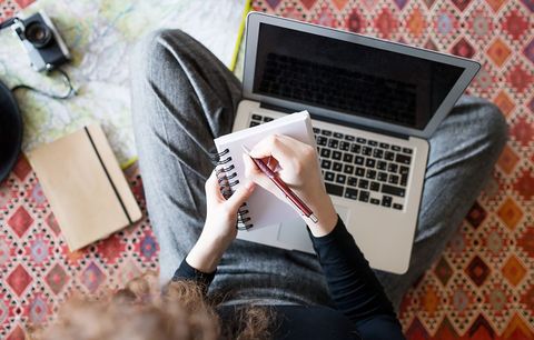 Student writing on a notepad in front of a laptop