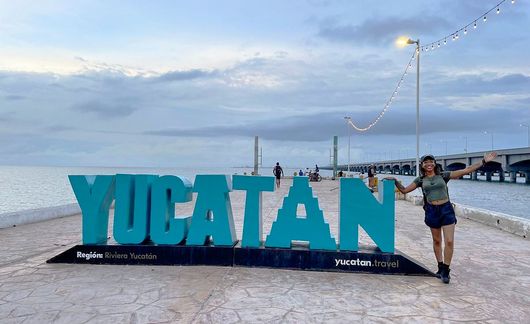 yucatan student posing by sign at beach