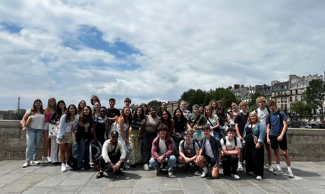 AM group posing for a photo on a bridge by the Seine, with the Eiffel Tower in the distance