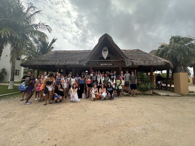Group of 50 students stands in front of the reception of the beach club