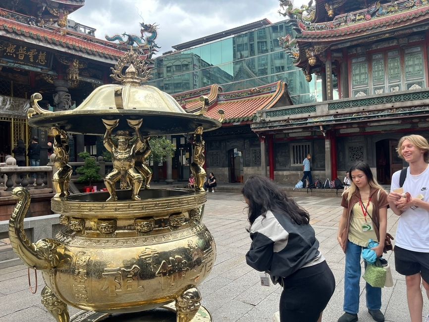 Group of students praying and getting their trinkets blessed by a large brass incense burner