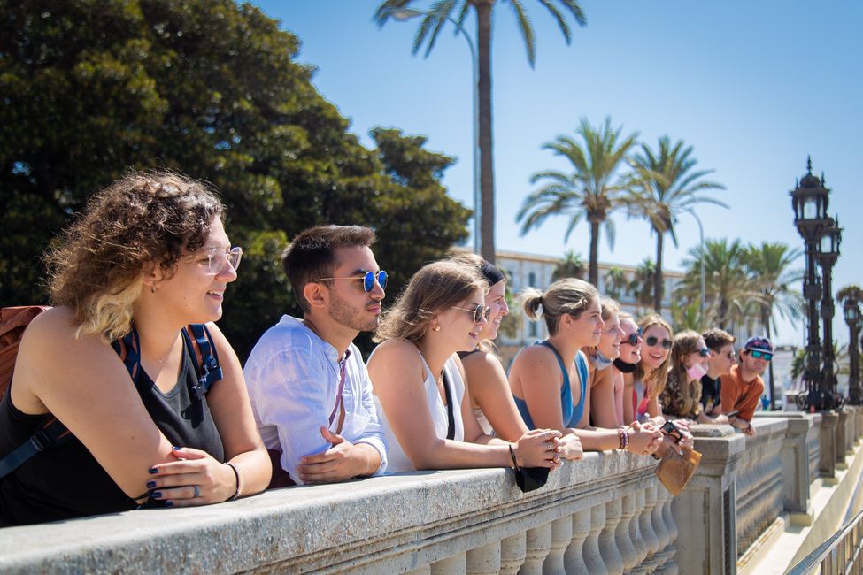 Students leaning on a balustrade facing La Caleta Beach in Cadiz