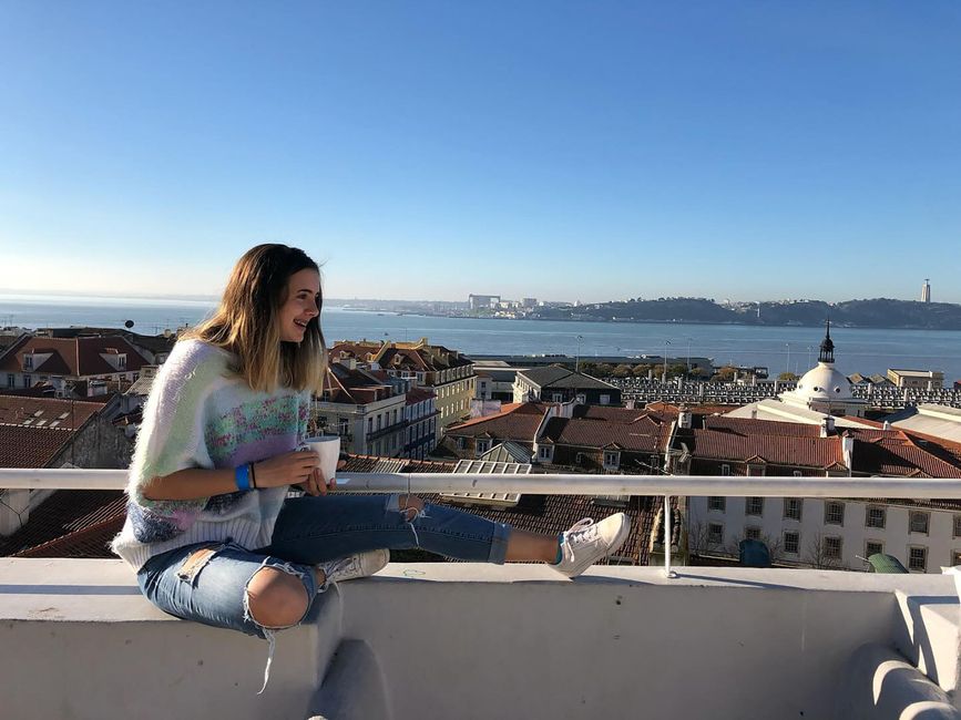 Student holding mug of tea while lounging on balcony above Spanish city