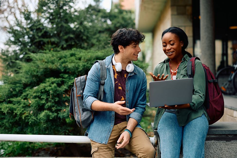 Two high school students talking outside while looking at laptop