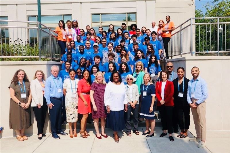 Group photo of participants, organizers, and special guests at the 2024 Young Civic Leadership Summit. The diverse group, wearing blue CIEE t-shirts, stands together on the steps outside a building, smiling and celebrating the successful event.