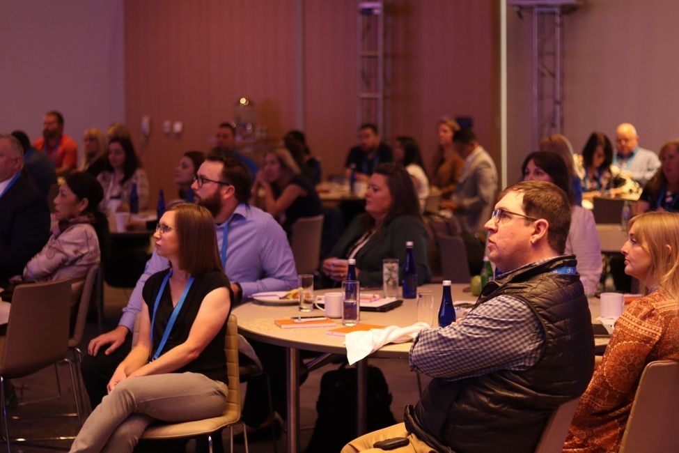 A crowd of people sit and listen to a panel discussion