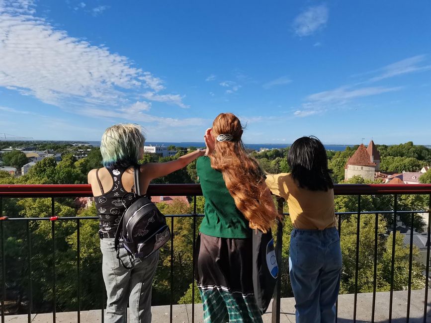 Three students leaning on balustrade looking at cityscape