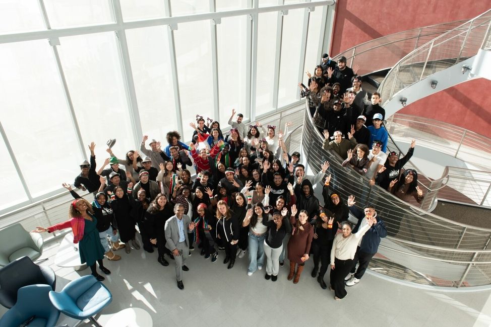 A group of 50 BMCC students and administrators standing in front of a spiral staircase and smiling up at the camera