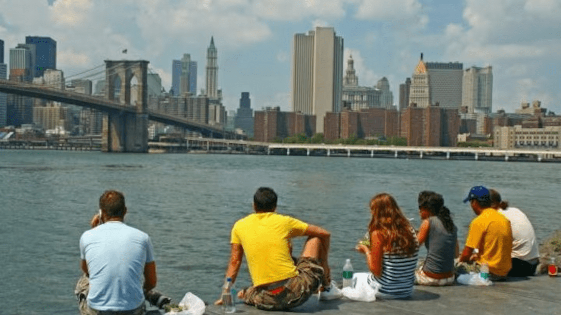 Students sit with their back towards the camera overlooking the Brooklyn Bridge and Manhattan