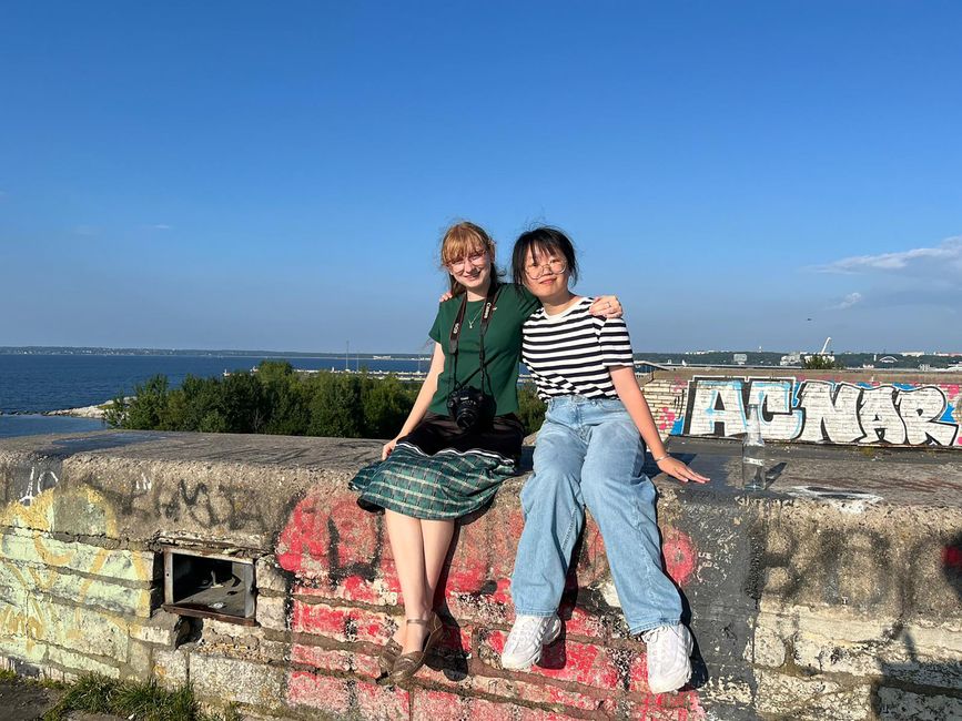 Two high school abroad students sitting on wall by the sea