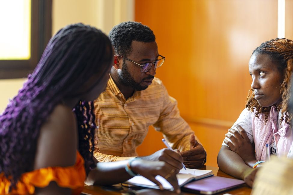 a male student with a notebook talking with intention to two female students