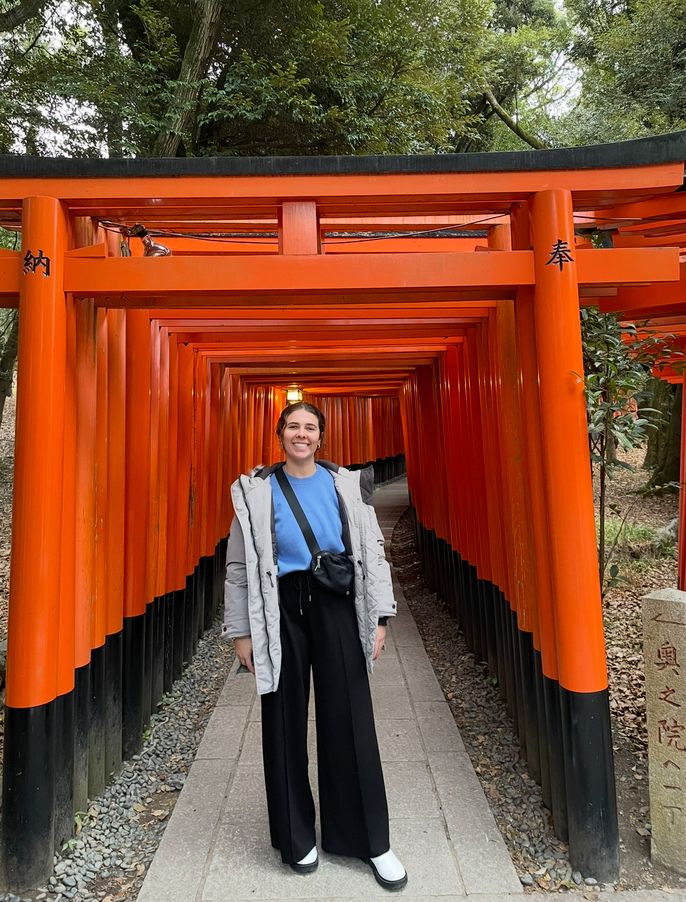 girl standing below the orange Torii Gates in Japan