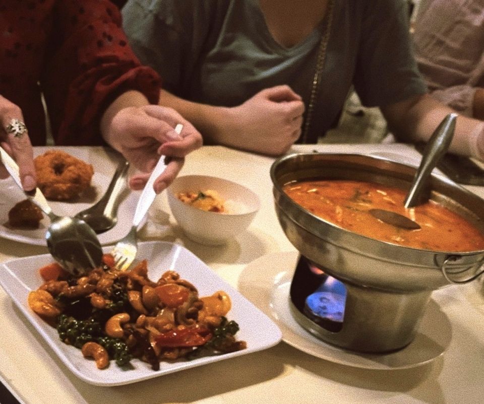 A dinner table with three people getting food from a plate of sweet and sour chicken and orange soup on a hot plate.