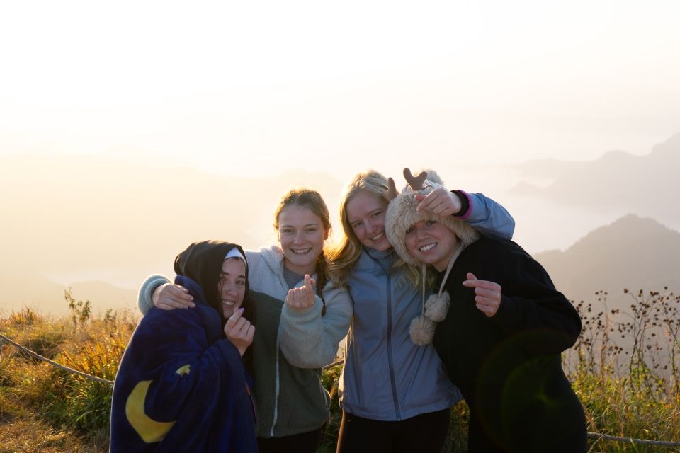 4 girls show "mini hearts" with mountains and clouds in the background. 