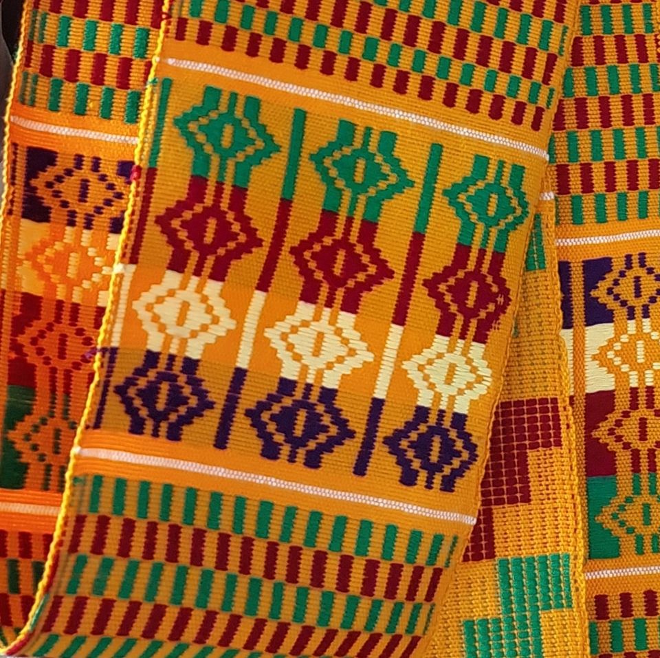 A strip of Kente (woven textile of the Asante people of Ghana) with a message. The colors are mostly red, green and yellow.