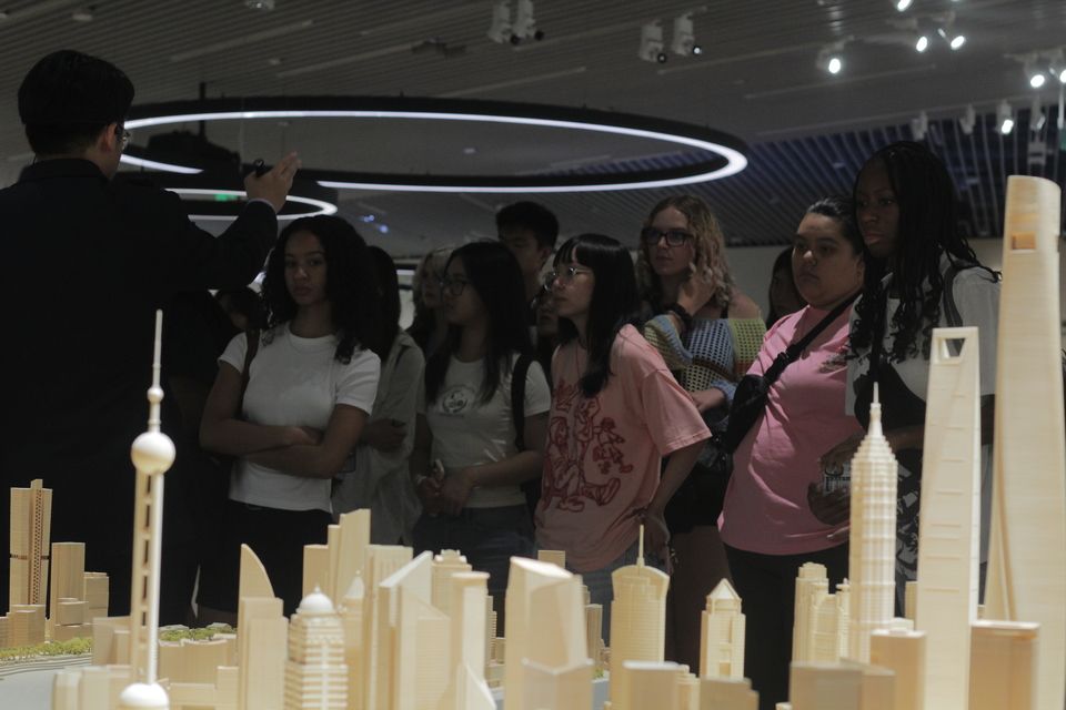 Behind a scaled version of Shanghai's The Bund, CIEE students look at their tour guide whose hand is raised in motion