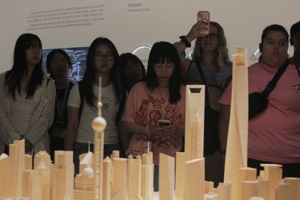 Seven students admire a scaled version of The Bund in Shanghai; one student on the far right raises her phone to take a photograph.