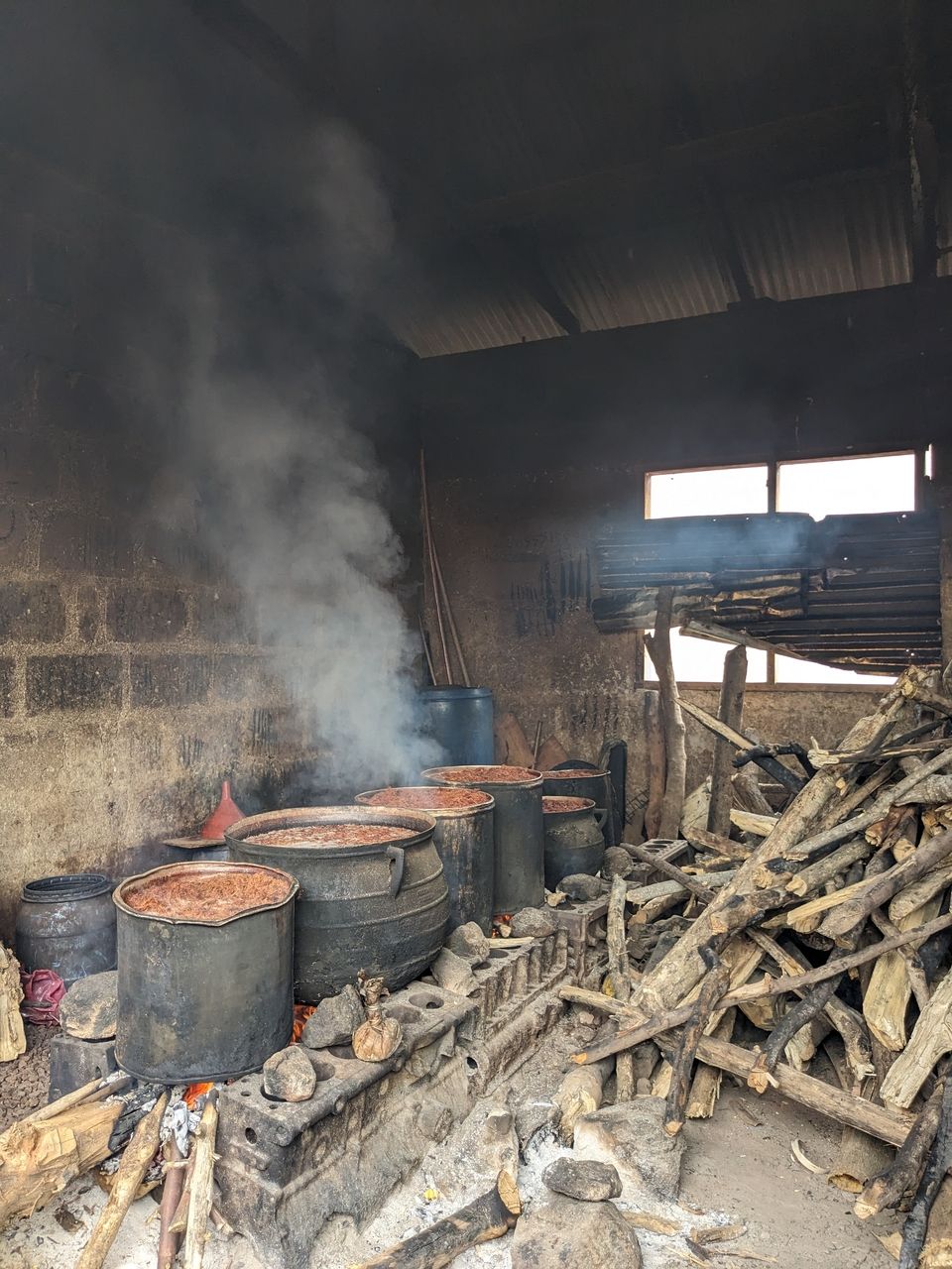 Pounded tree bark left on fire to boil in pots. In the makeshift kitchen is also a pile of firewood used for making fire. Boiling the pounded tree bark produces dye.