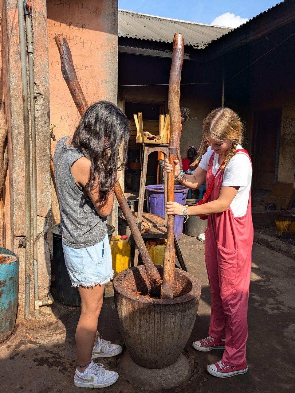 Two students try their hands on pounding the bark of the dye producing tree in preparation for boiling.