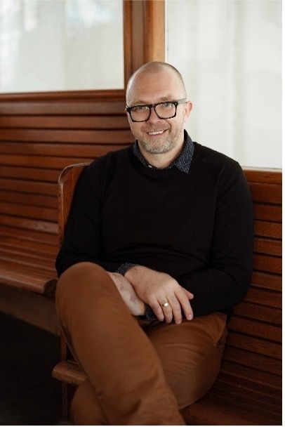 Vaidas sitting in a black sweater on a brown bench smiling - portrait shot