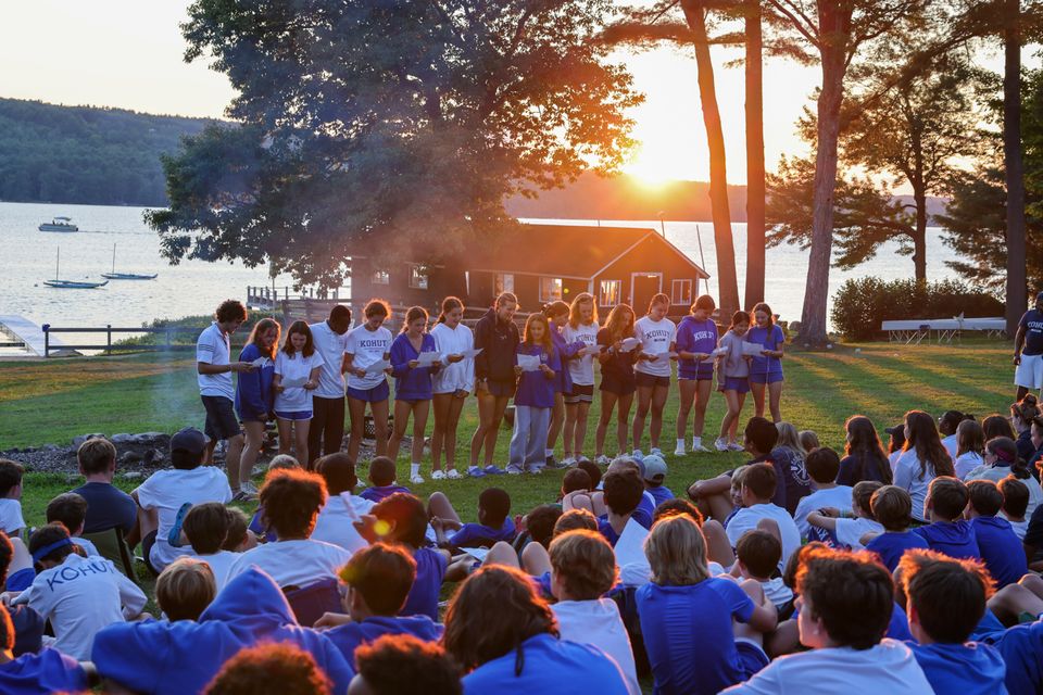 BridgeUSA participants standing in a line facing a group of younger students, outside by a lake. All wearing matching camp T-shirts.