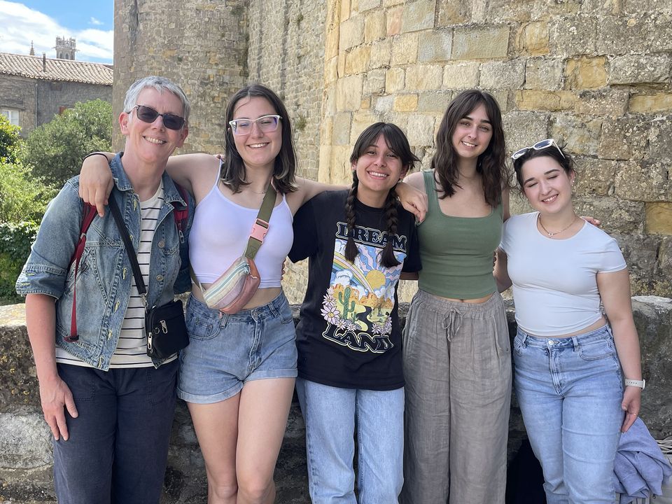 Group of high schoolers and program leader posing in front of stone building